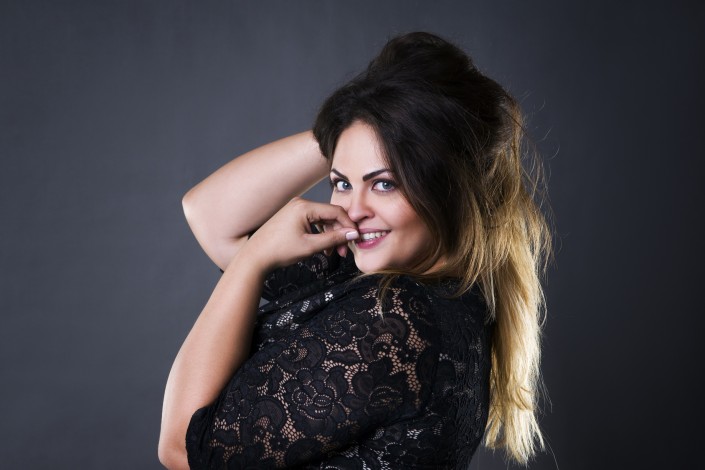 Young beautiful plus size model in black lace dres, xxl woman portrait on gray studio background