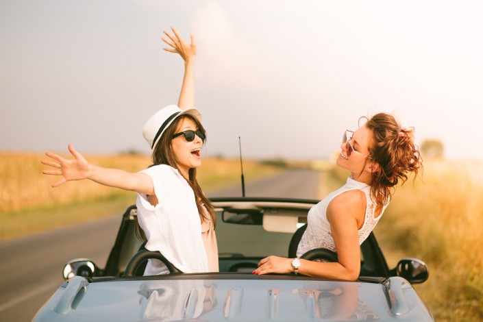 Two happy female friends enjoying road trip in their cabriolet