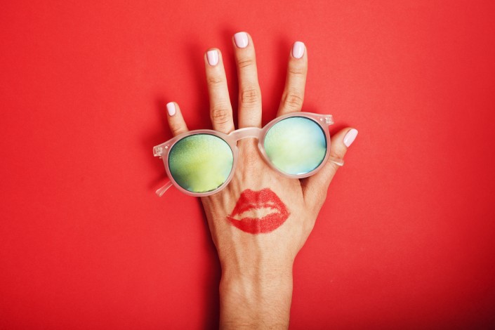 woman hand holding sunglasses on bright background, cosmetic summer vacation concept