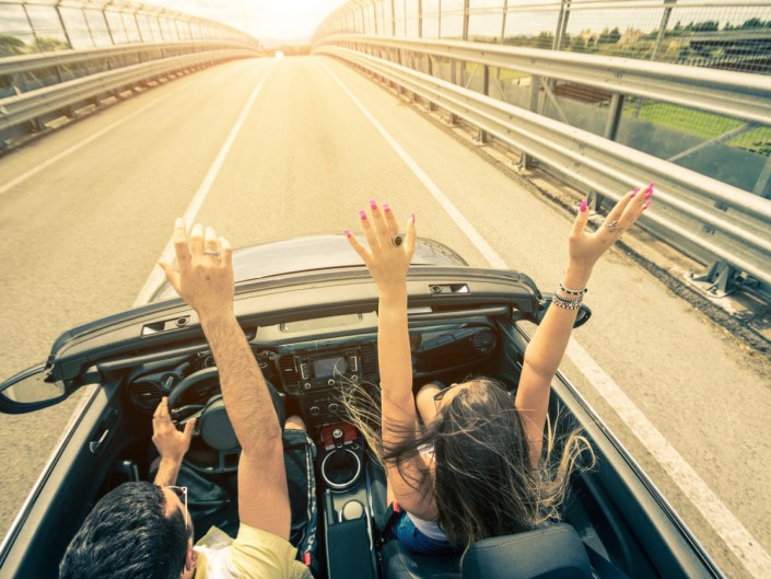 Happy couple driving on the road into the sunset in a sports car