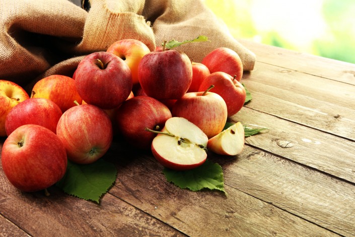 Ripe red apples with leaves on wooden background