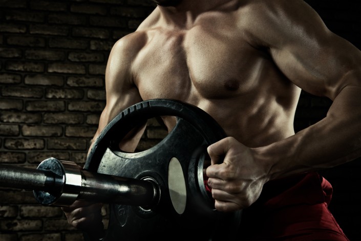 Sports background. Closeup photo of handsome bodybuilder guy prepare to do exercises with barbell in a gym, keep barbell plate in hands