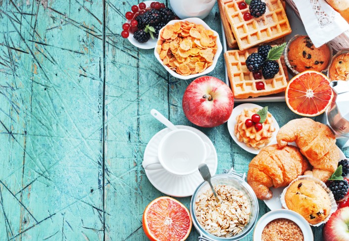 Healthy and colorful breakfast – cup of coffee with homemade granola, waffles, muffins,almond,hazelnuts,various fresh fruits, berries and milk on old wooden table.