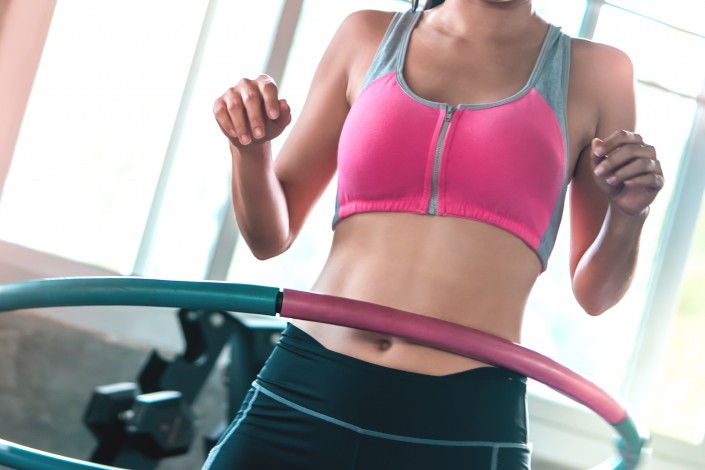 unrecognized Female in pink sportwear is working out with Hula hoop in fitness gym for healthy lifestyle concept