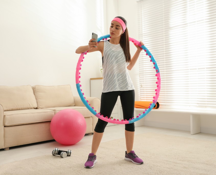 Lazy young woman with hula hoop and smartphone at home