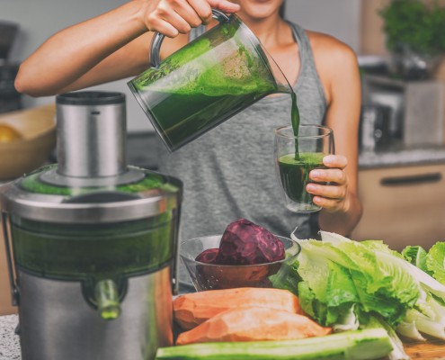 Woman juicing making green juice with juice machine in home kitchen. Healthy detox vegan diet with vegetable cold pressed extractor to extract nutrients for smoothie drink.
