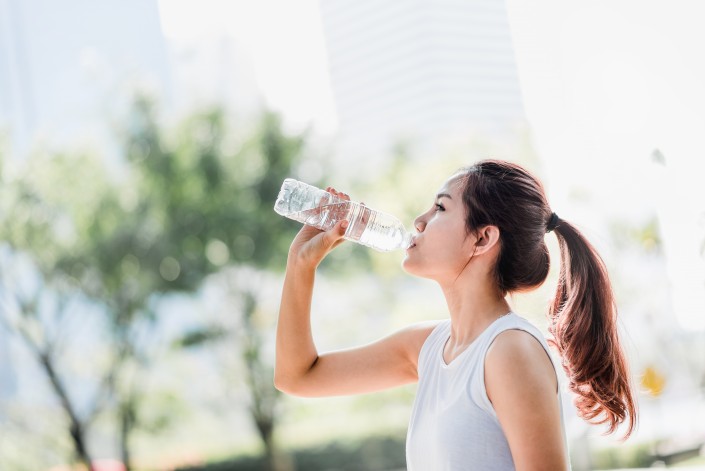 Shot of a young Asian woman drinking water from water bottle after jogging in the park.