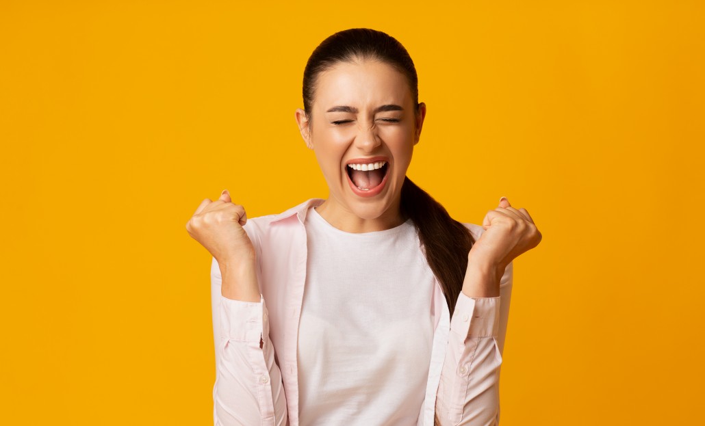 Woman Shouting Loudly And Shaking Clenched Fists On Yellow Background