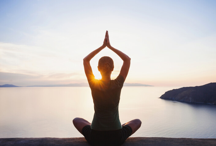Young woman practicing yoga near the sea at sunset. Harmony, meditation and travel concept. Healthy lifestyle