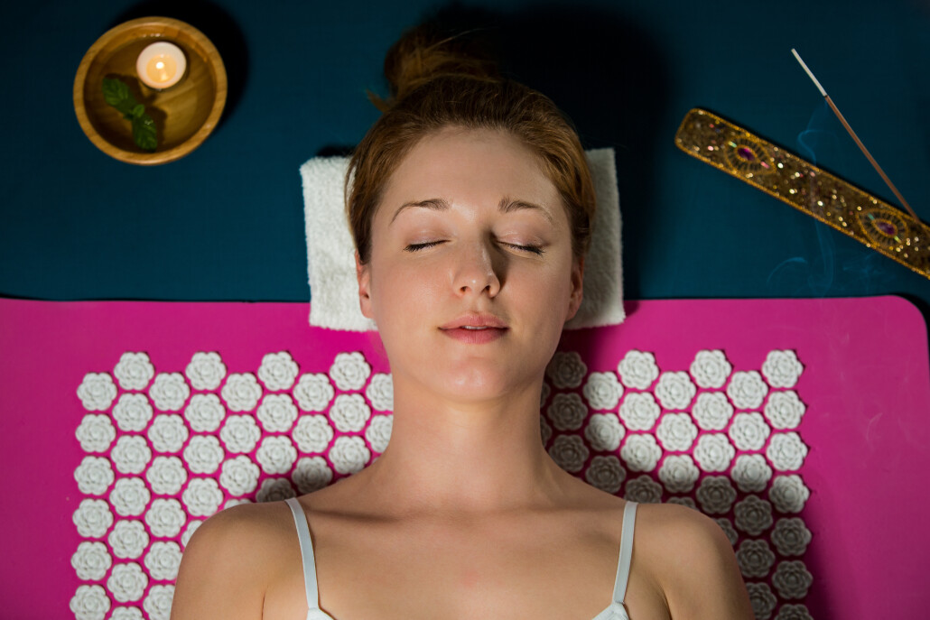 Woman with closed eyes Relaxing at home, lying on acupuncture mat. Candles and incense aroma sticks.