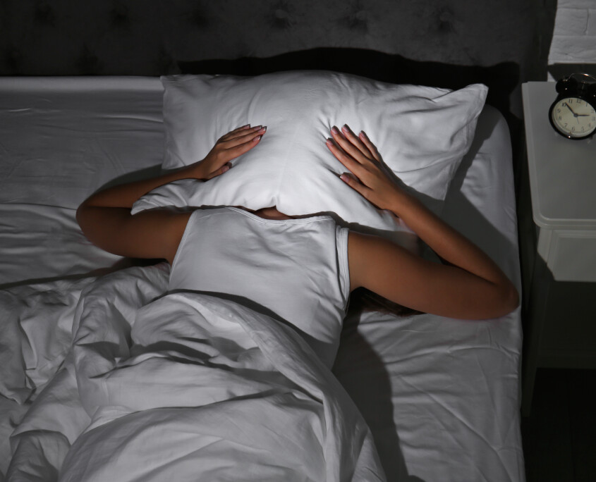 Young woman covering head with pillow in bed at home. Sleep disorder
