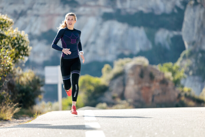Sporty young woman running on mountain road in beautiful nature.