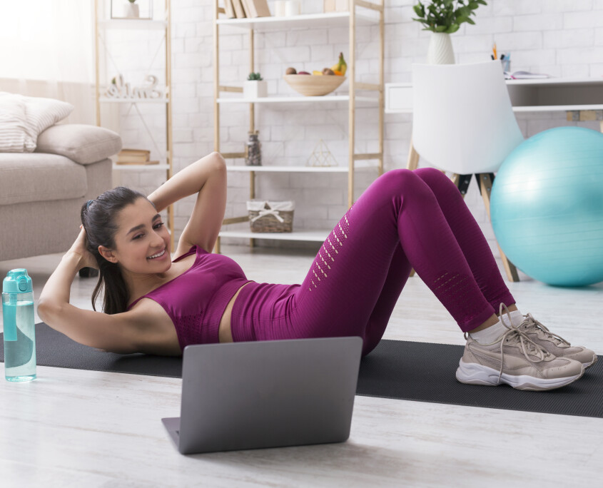 Lockdown sports. Sporty girl doing abs exercises to online workout video at home
