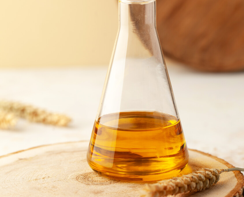 Organic vegetable oil in a glass flask on a wooden stand with spikelets of wheat with space for text. Vertical photo.